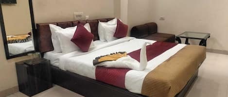 Un lit bien fait, recouvert d’une couverture marron, agrémenté d’oreillers blancs et rouges, et d’un coussin décoratif en forme de cygne. Une petite table avec un plateau en verre se trouve à côté du lit.