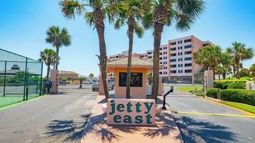 A sign for 'Jetty East' with a small kiosk, palm trees, and a tennis court in the background.