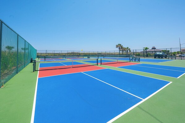 Un terrain de tennis comprenant plusieurs courts, une clôture et un bâtiment en arrière-plan.