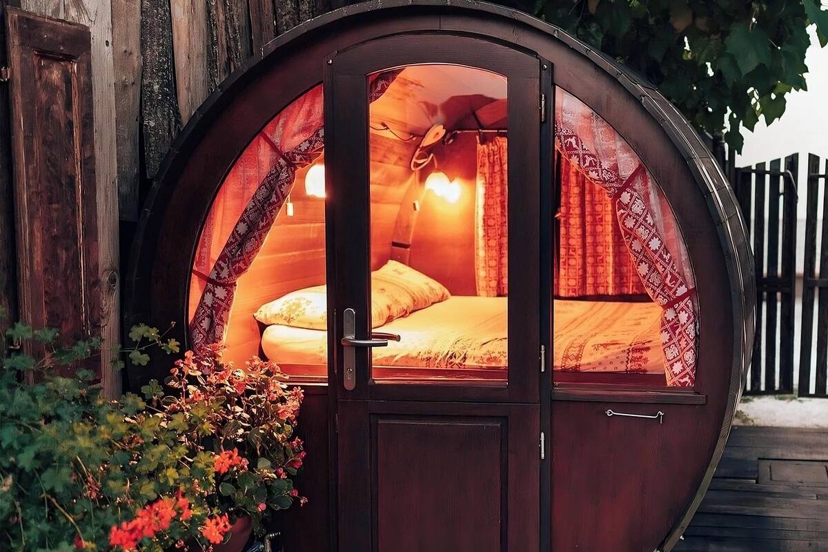 A cozy, round wooden structure with a bed inside, featuring curtains and a window.