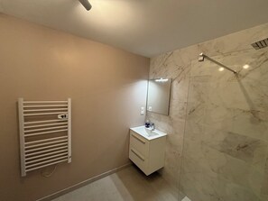 Un baño con tocador blanco, espejo, toallero y zona de ducha con azulejos de mármol.