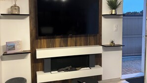 Un salon moderne avec un téléviseur à écran plat fixé à un mur en bois, une cheminée en dessous et une petite table avec une télécommande.