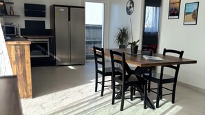 Une cuisine moderne équipée d’un four encastré, d’un réfrigérateur et d’un coin repas avec une table et des chaises en bois.