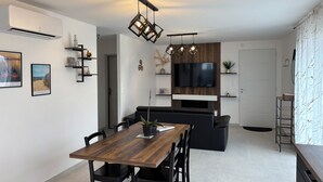 Une cuisine moderne dotée d’un four encastré, un coin repas avec une table et des chaises en bois, un canapé noir et un téléviseur fixé au mur.