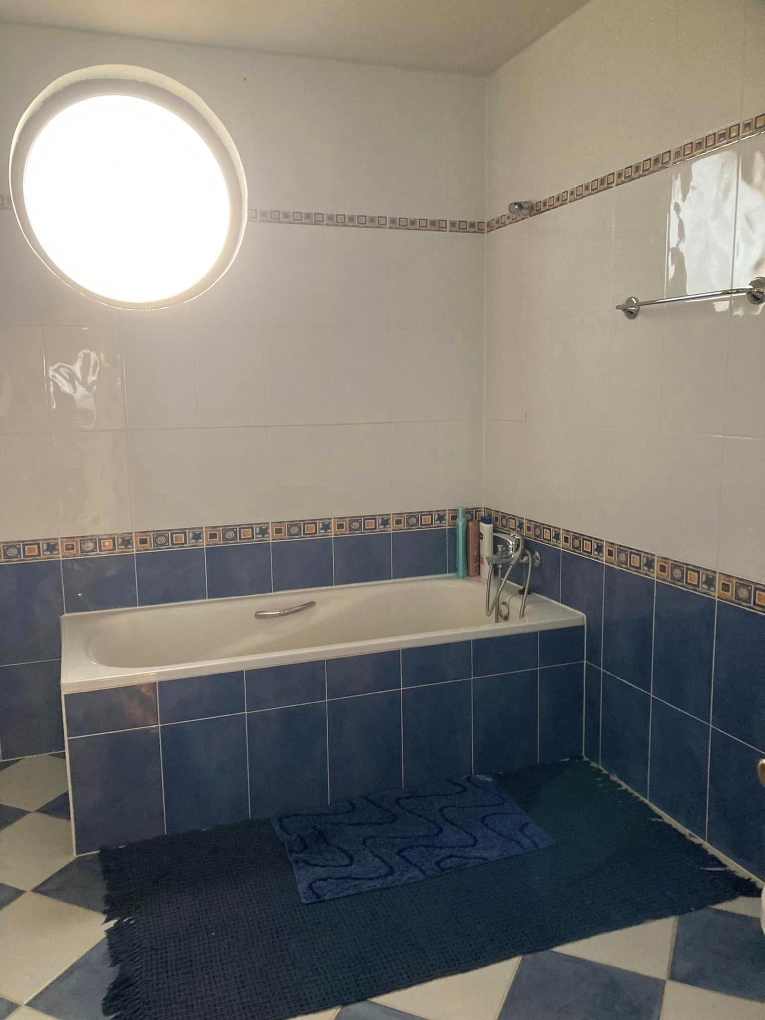 Une salle de bain avec une baignoire, un miroir rond et un porte-serviettes.