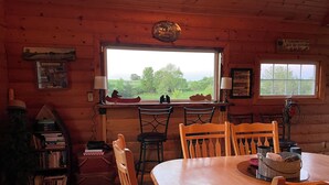 A cozy cabin interior with a dining table, chairs, a bookshelf, and a window offering a view of greenery. - Little Lake Louise (Lucas)