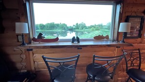 A cabin interior with a large window overlooking a lake, two chairs, and a lamp on each side. - Little Lake Louise (Lucas)