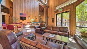 A spacious indoor area with wooden walls, a pool table, leather sofas, and a large window providing a view of the outdoors.