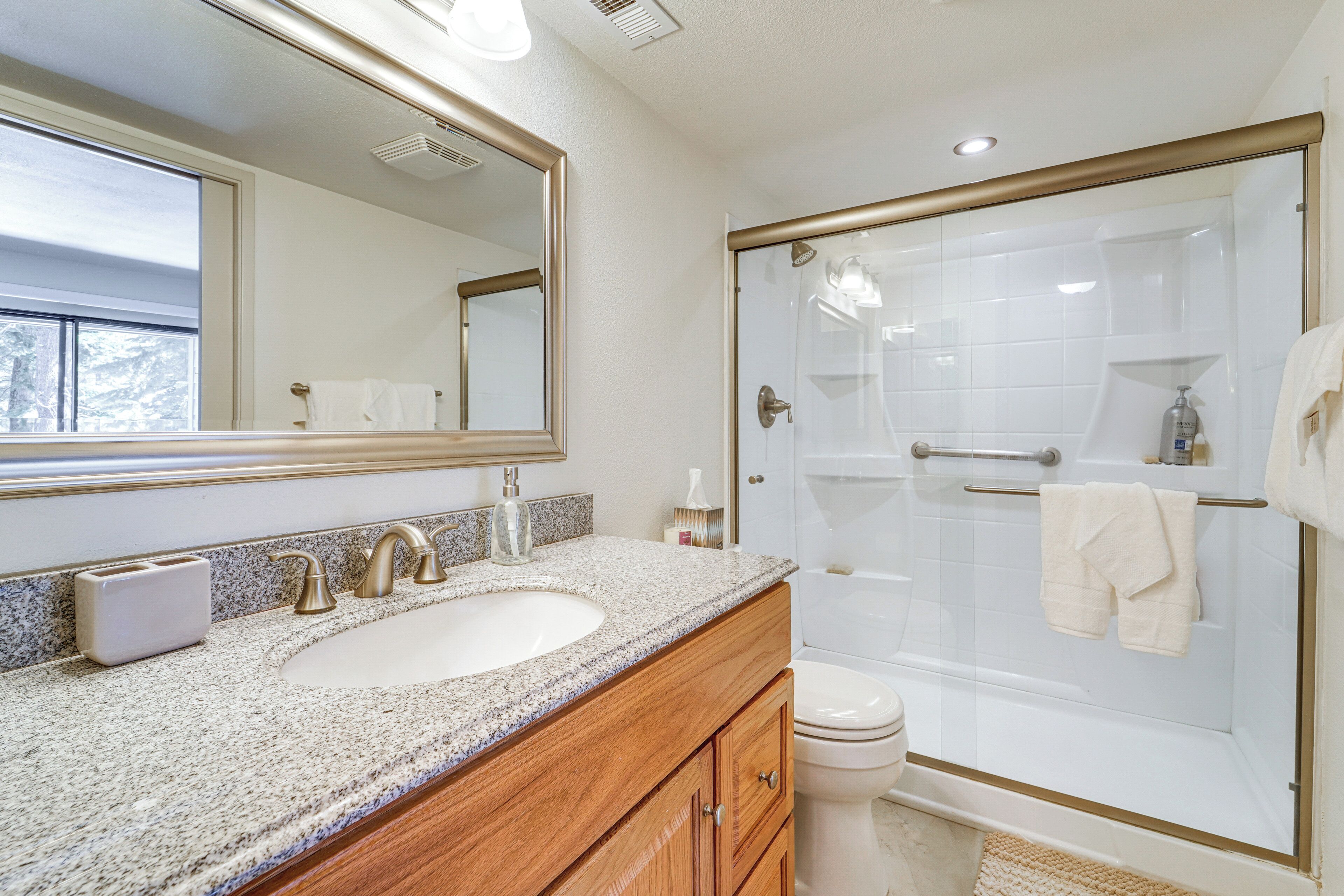 Un baño con lavamanos de encimera de granito, un espejo, un inodoro y una ducha con cerramiento de vidrio.