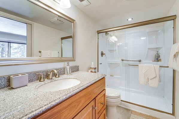 A bathroom with a granite countertop sink, a mirror, a toilet, and a glass-enclosed shower.