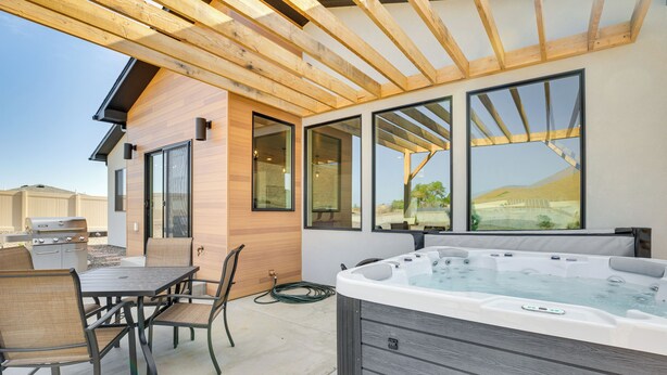 Een terras buiten met een hottub, een houten pergola en een eethoek met stoelen en een tafel.