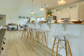 Eine moderne Küche mit einer zentralen Kochinsel, Holzstühlen, Pendelleuchten und weißen Schränken.