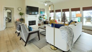 Un salon avec un canapé blanc, une table basse et un lampadaire. On y trouve une cheminée avec un manteau de cheminée et une horloge au mur.