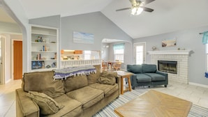A spacious living room with a high ceiling, a fireplace, a sofa, a coffee table, and a bookshelf.