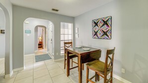 A dining area with a table and chairs, a colorful artwork on the wall, and a hallway leading to another room.