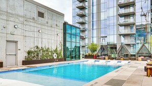 Piscina com placa de 'Não Mergulhar', rodeada por edifícios modernos e áreas de estar ao ar livre.