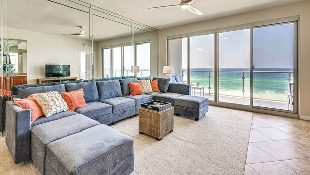 A spacious living room with a large gray sectional sofa, a wicker coffee table, and a ceiling fan. - Oceanfront Destin Condo With Pool & Beach Access (Destin)