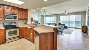 A modern kitchen with wooden cabinets, a built-in microwave, and an oven. There is a large window offering a view of the ocean. - Oceanfront Destin Condo With Pool & Beach Access (Destin)