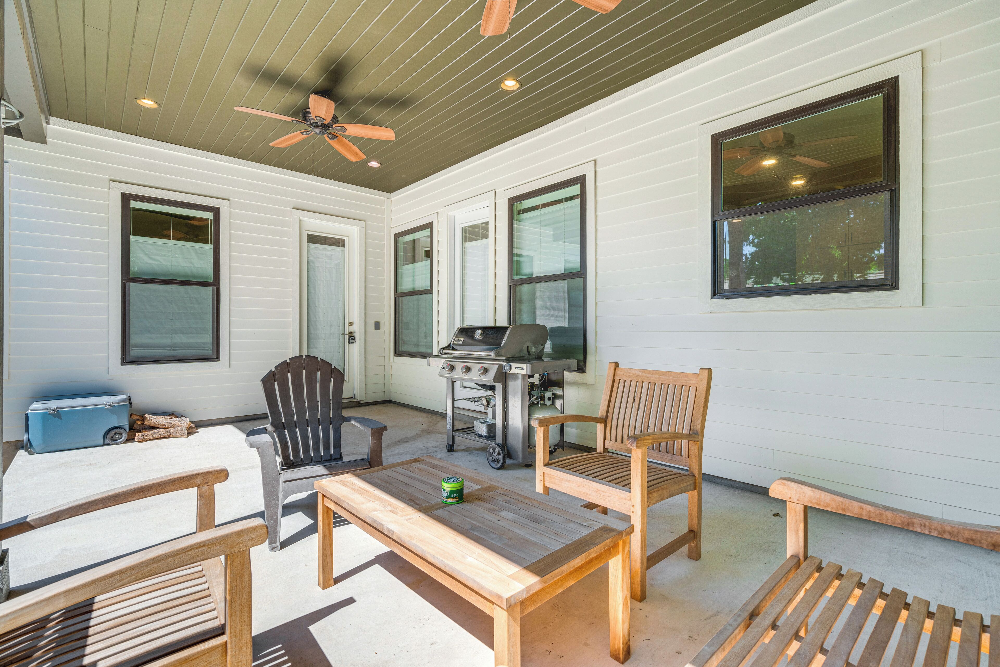 A covered patio area with a ceiling fan, a grill, and seating arrangements including chairs and a table.