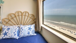 A room with a bed, a window with a view of the beach, and a wall with a decorative item. - Shore & Pool Access: Resort Condo in Myrtle Beach! (Myrtle Beach)