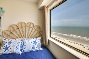 Een kamer met een bed, een raam met uitzicht op het strand en een decoratief object aan de muur.