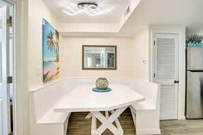 Una mesa de comedor blanca con un jarrón decorativo, un espejo enmarco y un cuadro de una playa.
