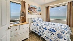 A bedroom with a bed, a nightstand, a lamp, a dresser, and a painting of a coastal scene. - Shore & Pool Access: Resort Condo in Myrtle Beach! (Myrtle Beach)