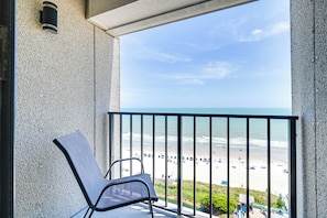 Een balkon met uitzicht op een strand, een stoel en een gebouw in de verte.
