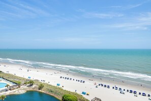 A beach with umbrellas and lounge chairs, a pool, and a clear view of the ocean.