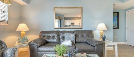 A living room with a leather sofa, a glass coffee table, and a large mirror.