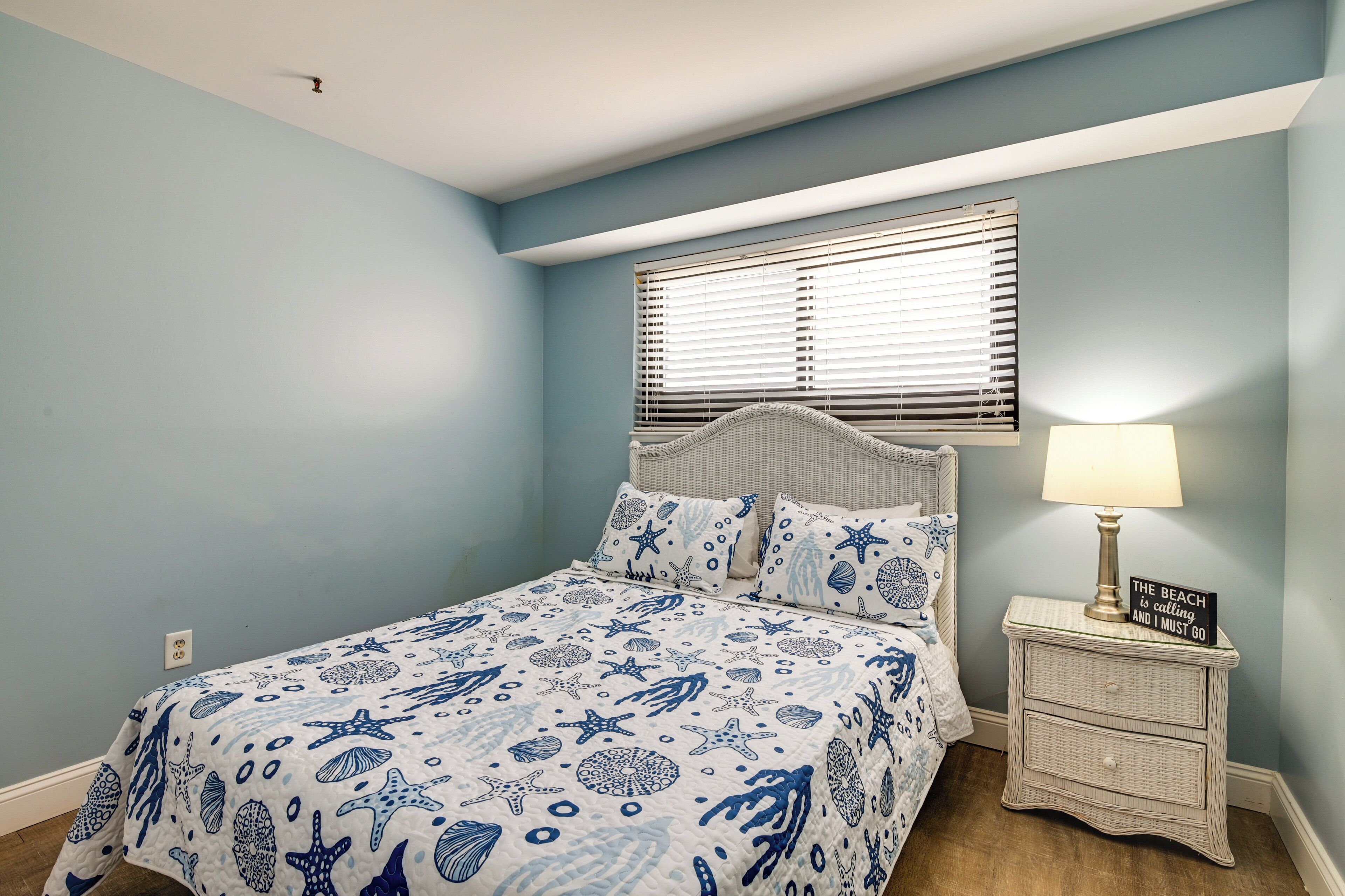 A bedroom with a bed, a nightstand with a lamp, and a window with blinds.