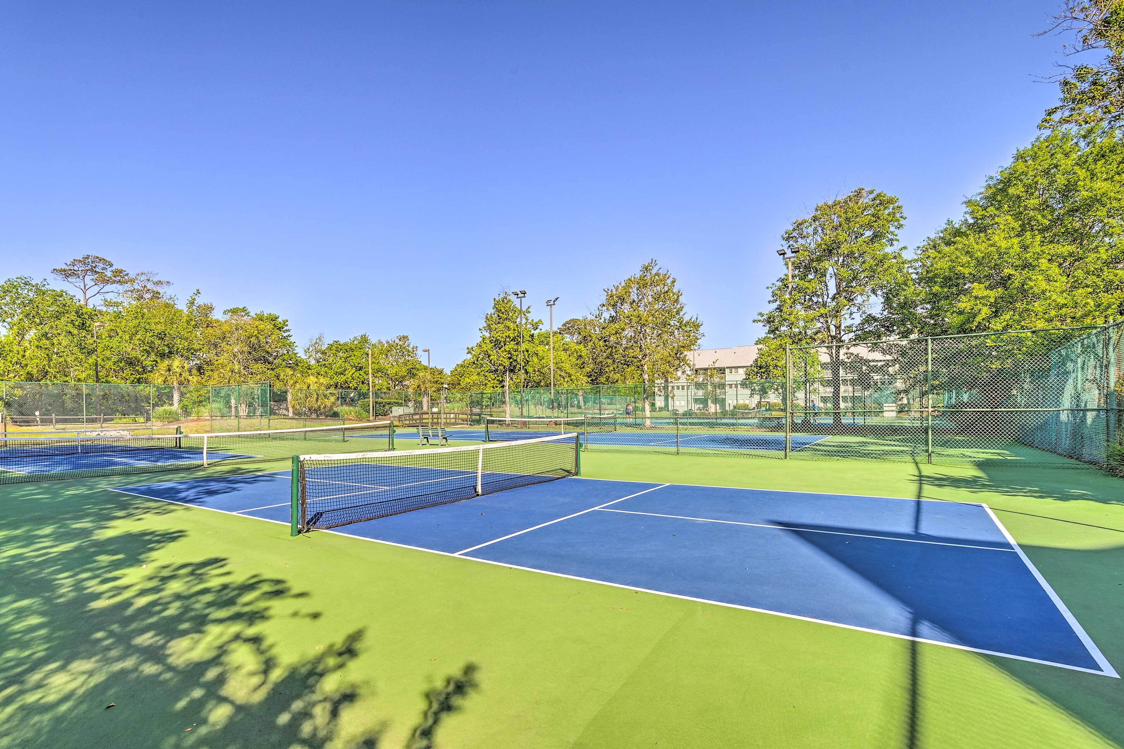 A tennis court with a net, surrounded by trees and a fence.