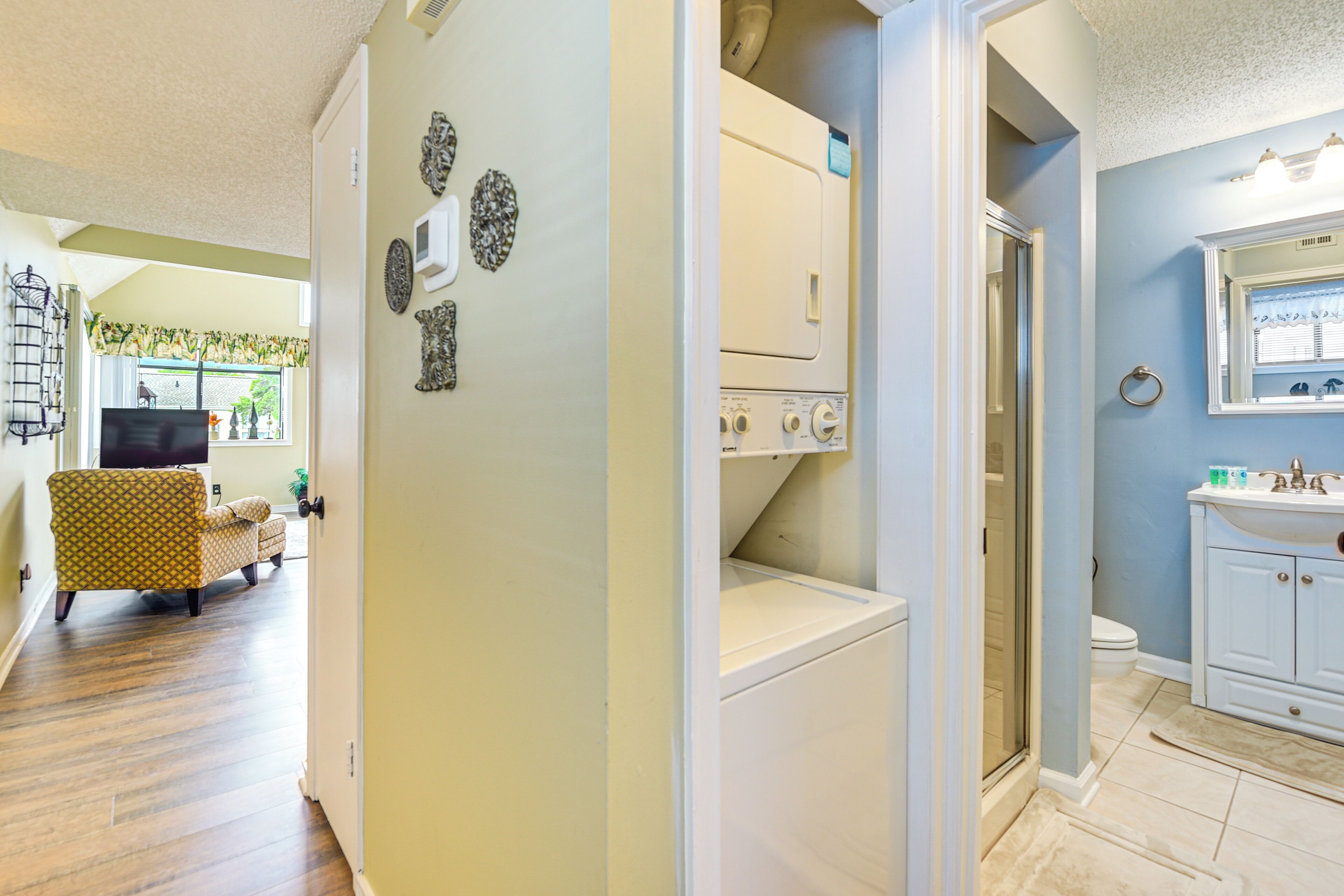 A laundry room with a washing machine and dryer, a bathroom with a sink and mirror, and a living area with a patterned armchair and television.