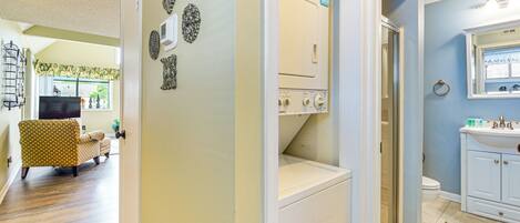 A laundry room with a washing machine and dryer, a bathroom with a sink and mirror, and a living area with a patterned armchair and television.