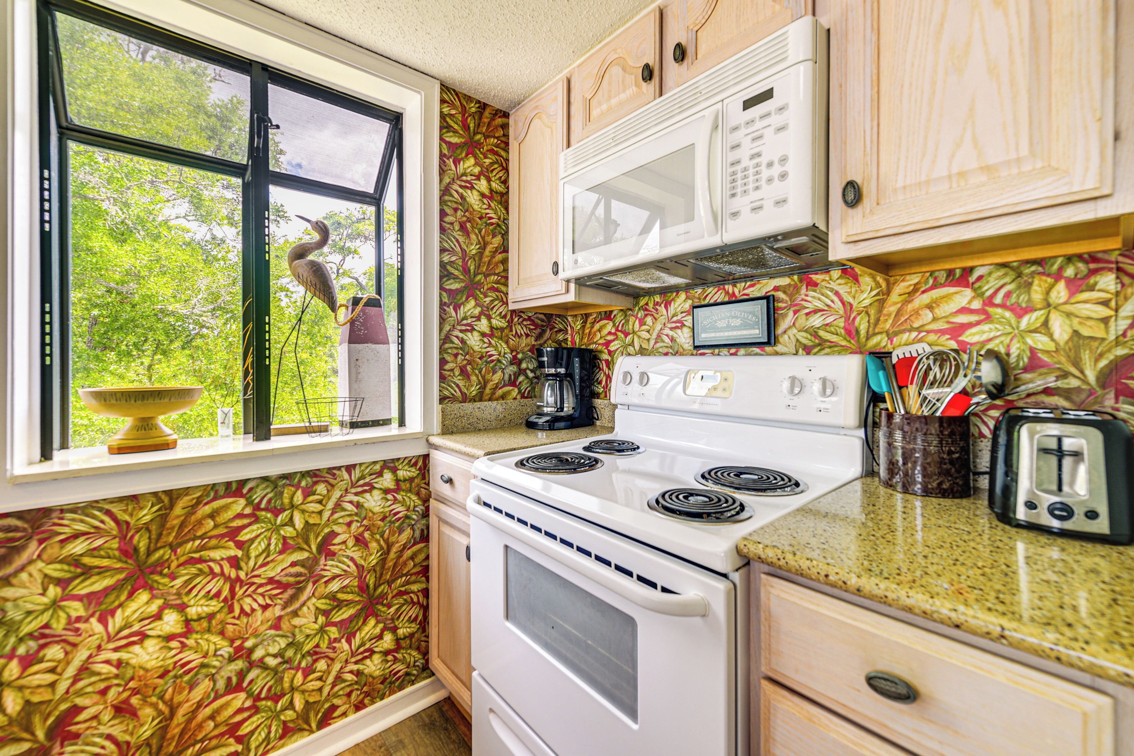 A kitchen with a white stove, a microwave, and a window with a view of trees.