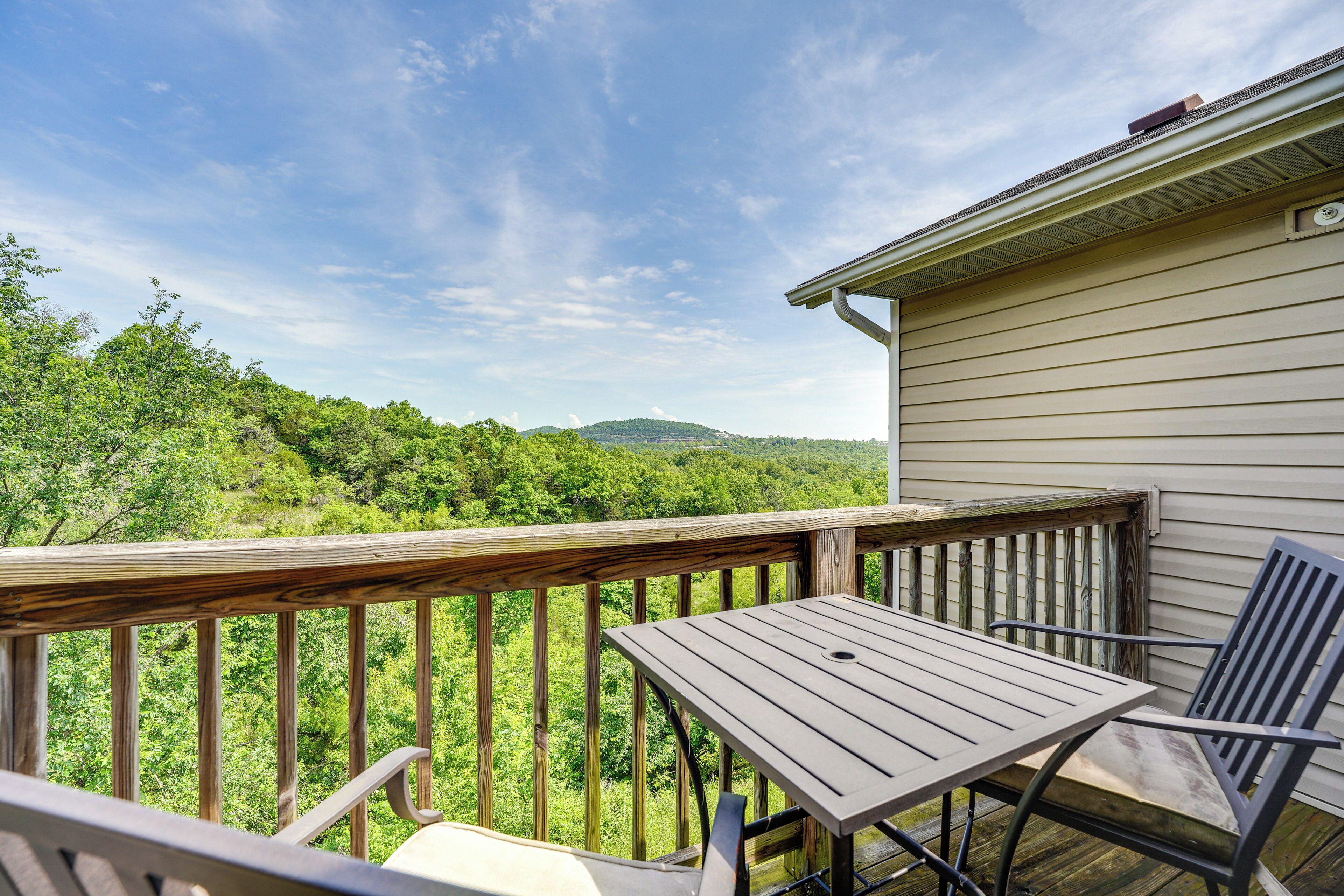 A wooden deck with a table and chairs, overlooking a lush green landscape and hills.