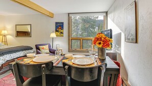 Un coin repas avec une table dressée pour deux personnes, un canapé et une fenêtre donnant sur les arbres.