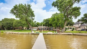 A wooden dock leading to a house with a covered porch, surrounded by trees and a calm body of water. - Private Dock & Deck: Eagle Mountain Lake Retreat! (Newark)