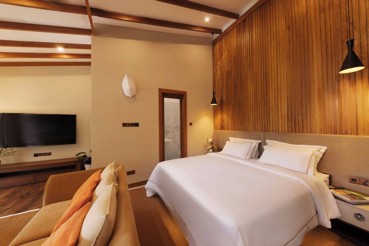 Quarto de hotel com uma cama grande, uma TV de tela plana, uma parede de destaque em madeira e uma luminária moderna.