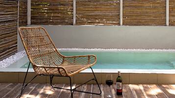 Una silla de mimbre junto a una piscina con una botella de vino sobre una mesa de madera.