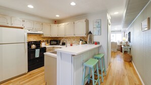 Une cuisine avec des meubles blancs, un îlot central doté de tabourets, un four à micro-ondes et une cuisinière.