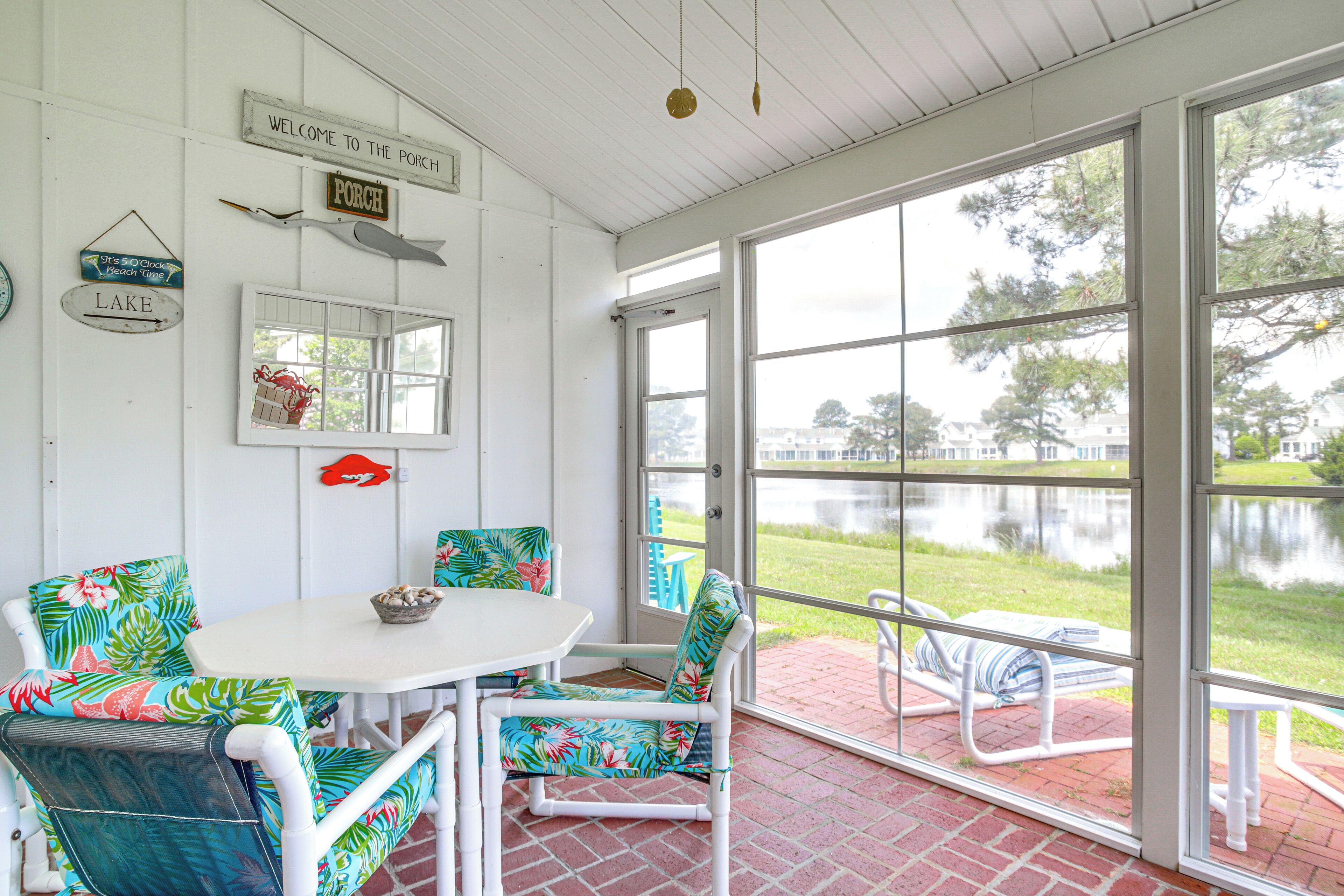 A covered patio with a table and chairs, a view of a lake, and signs indicating 'Welcome to the Porch' and 'Lake'.