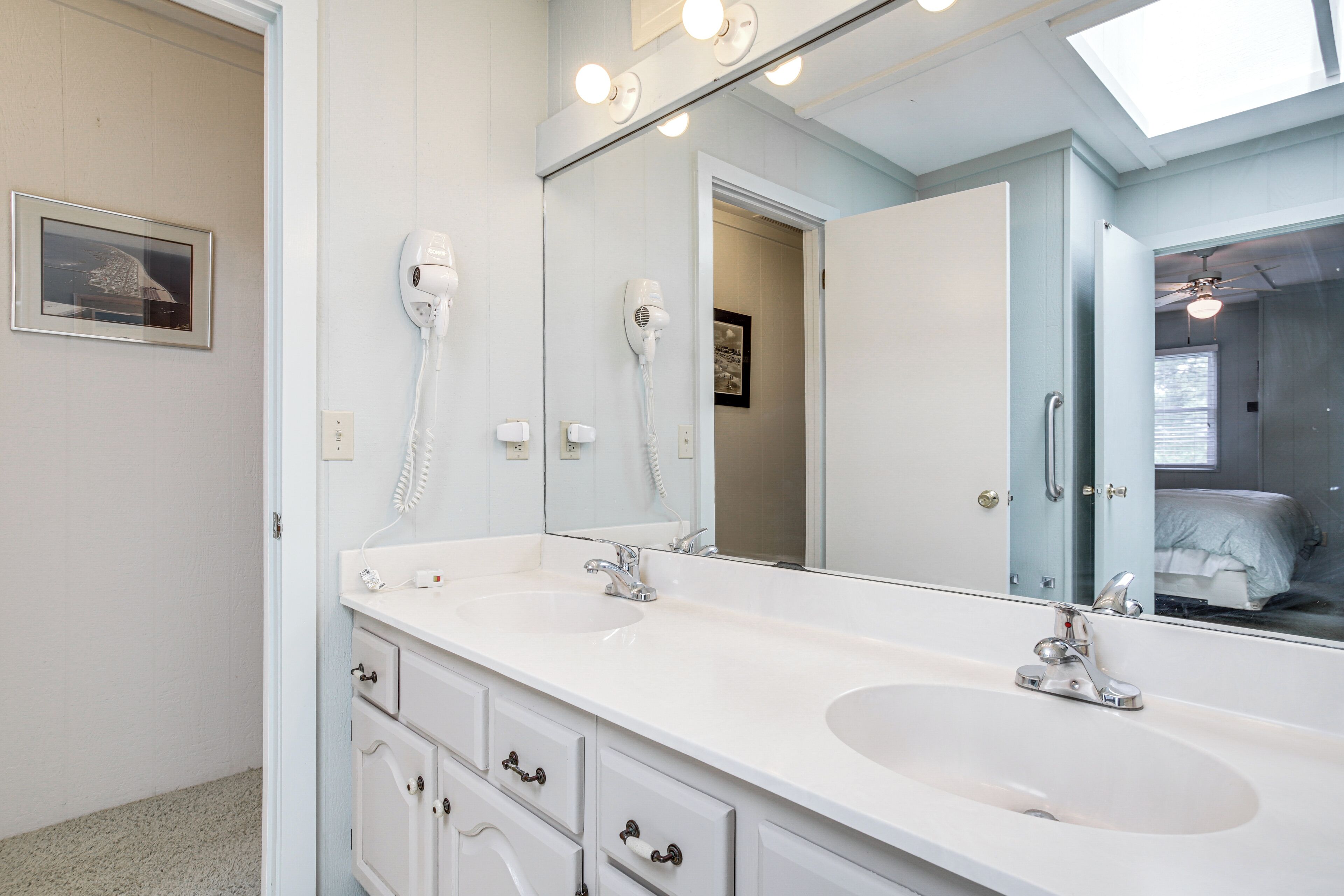 A bathroom with two sinks, a large mirror, and a hairdryer on the wall.