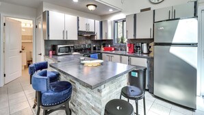 A modern kitchen with a central island, stainless steel appliances, and blue bar stools. - Hot Tub & Lake Beach Access: Tobyhanna Retreat! (Tobyhanna)