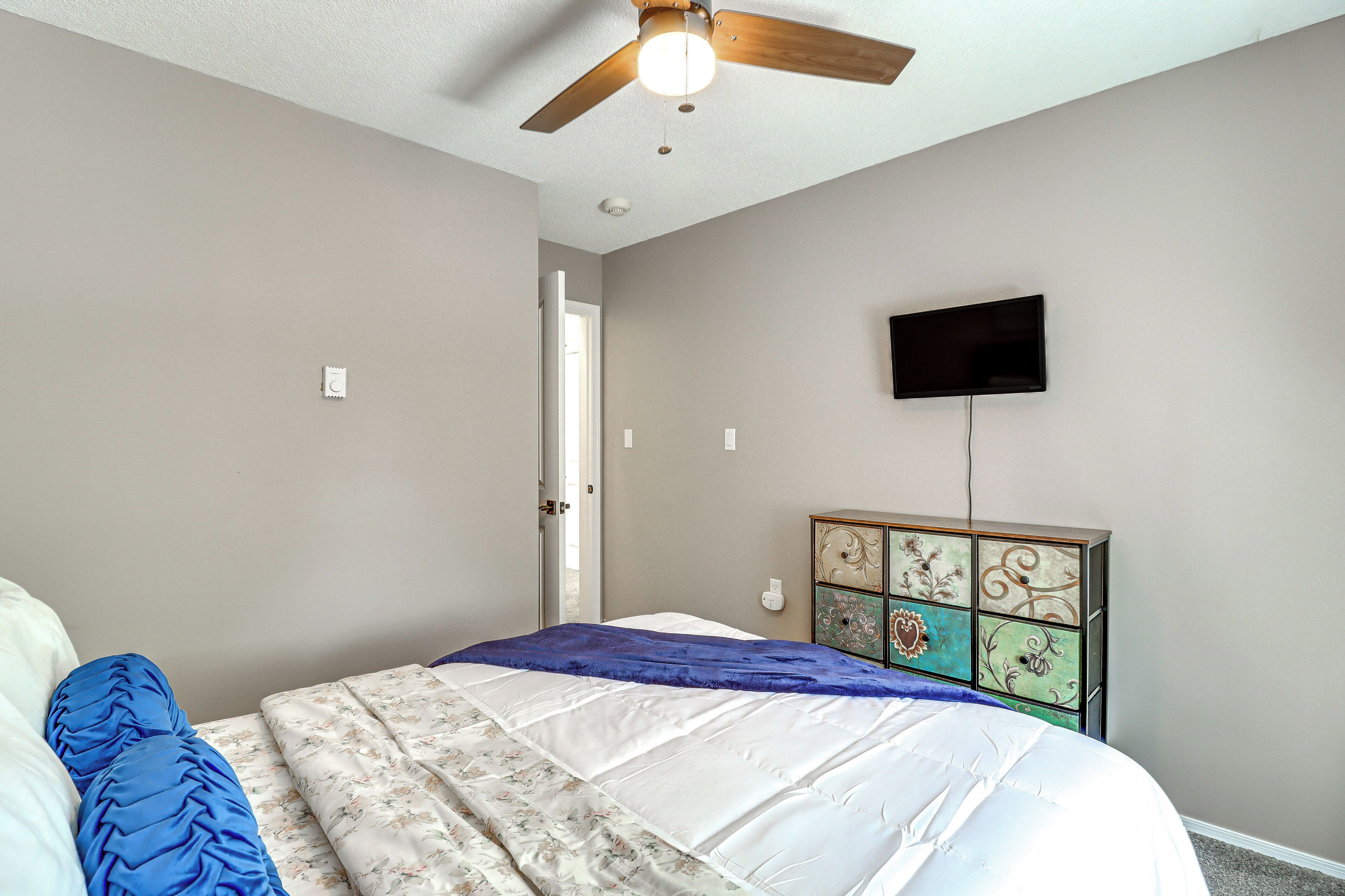 A bedroom with a bed, a ceiling fan, a television mounted on the wall, and a dresser with decorative panels.
