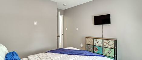 A bedroom with a bed, a ceiling fan, a television mounted on the wall, and a dresser with decorative panels.