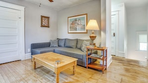 Un salon avec une table basse en bois, un canapé gris, une table d’appoint en bois avec une lampe et un ventilateur de plafond.