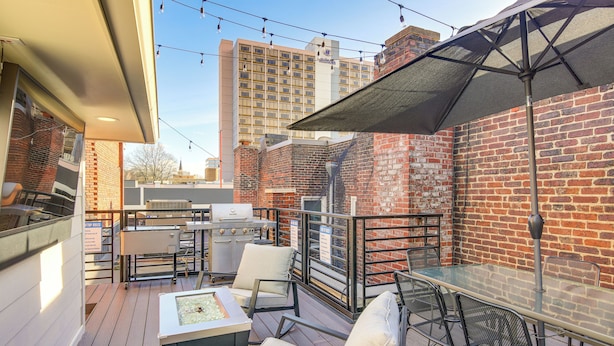 An outdoor patio with a glass table, metal chairs, a grill, and string lights. - Loft in the Heart of Dtwn Knoxville (Knoxville)