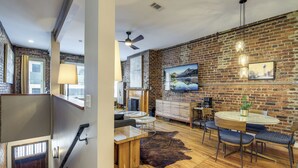 A spacious living area with a brick wall, a round dining table with blue upholstered chairs, a glass coffee table, and a leather rug. - Loft in the Heart of Dtwn Knoxville (Knoxville)