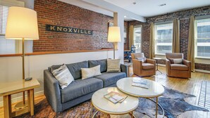 A cozy living room with a brick wall, a couch, two armchairs, a coffee table, and a rug. - Loft in the Heart of Dtwn Knoxville (Knoxville)